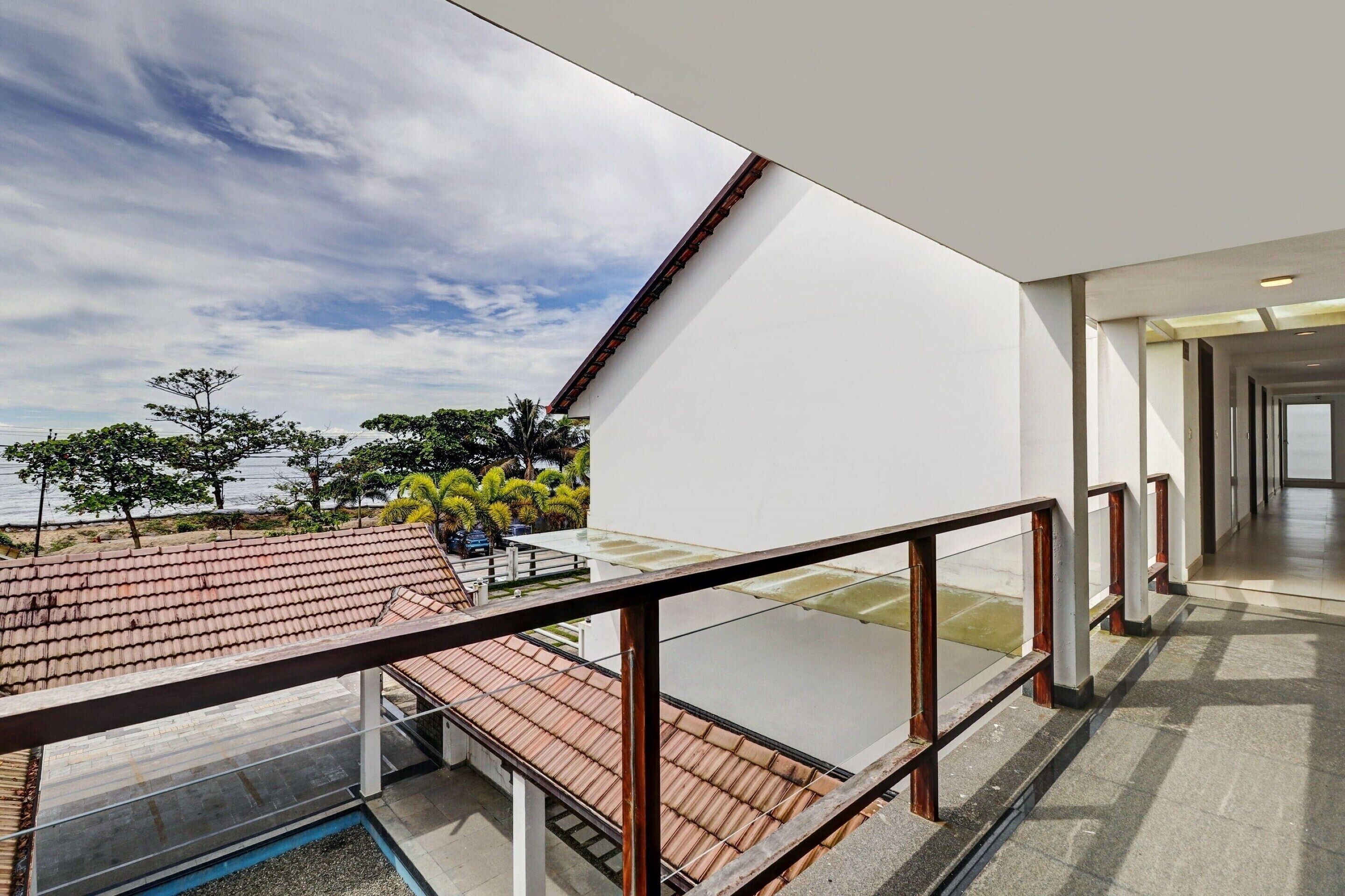 A modern building with a glass balcony overlooking a tiled roof and a body of water.
