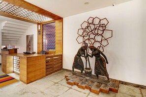 Zona de recepción con un escritorio de madera, un teléfono y una escultura mural de dos figuras.