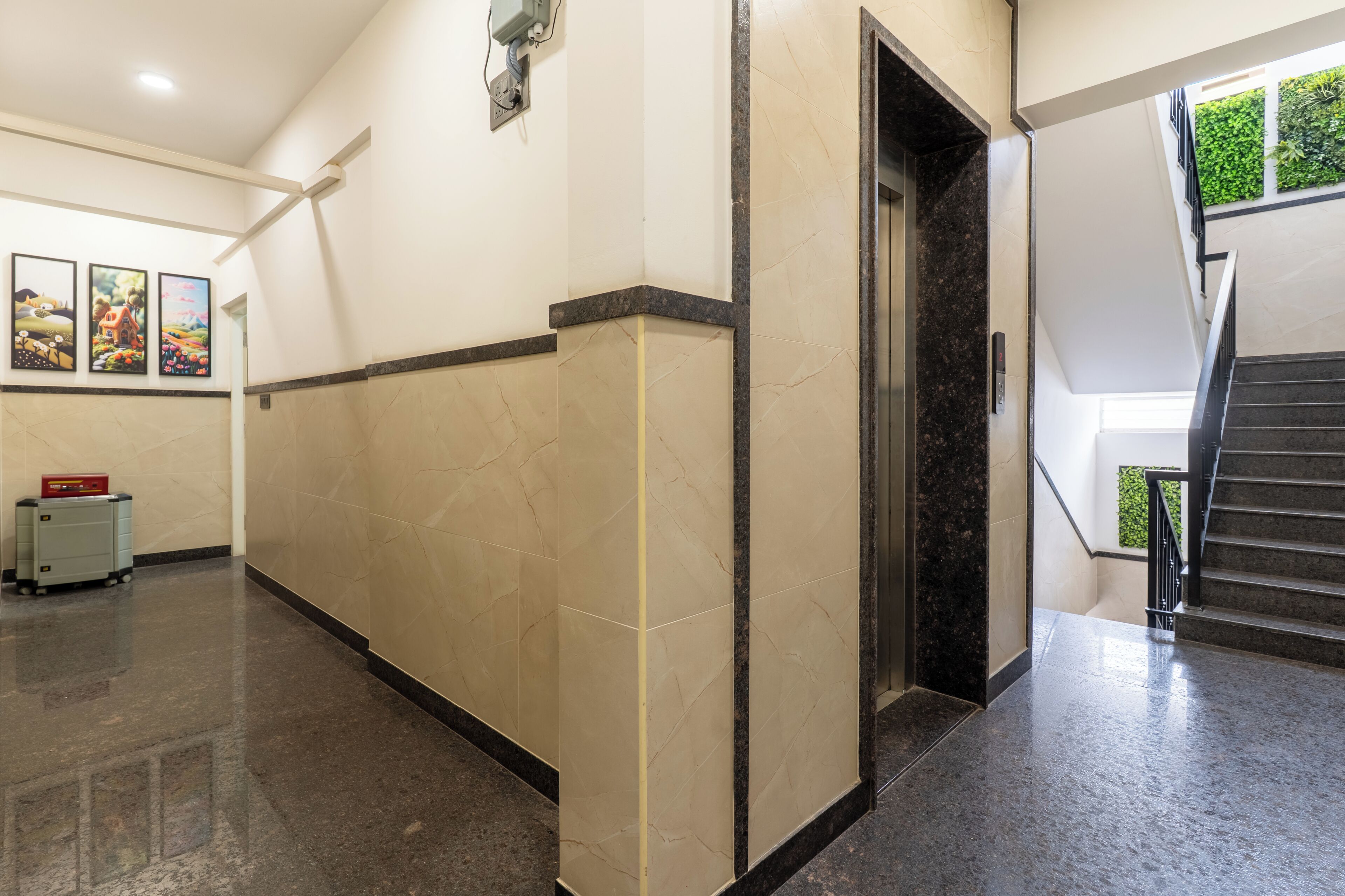 A hallway with a marble floor, a wall-mounted light fixture, and a staircase with a handrail.