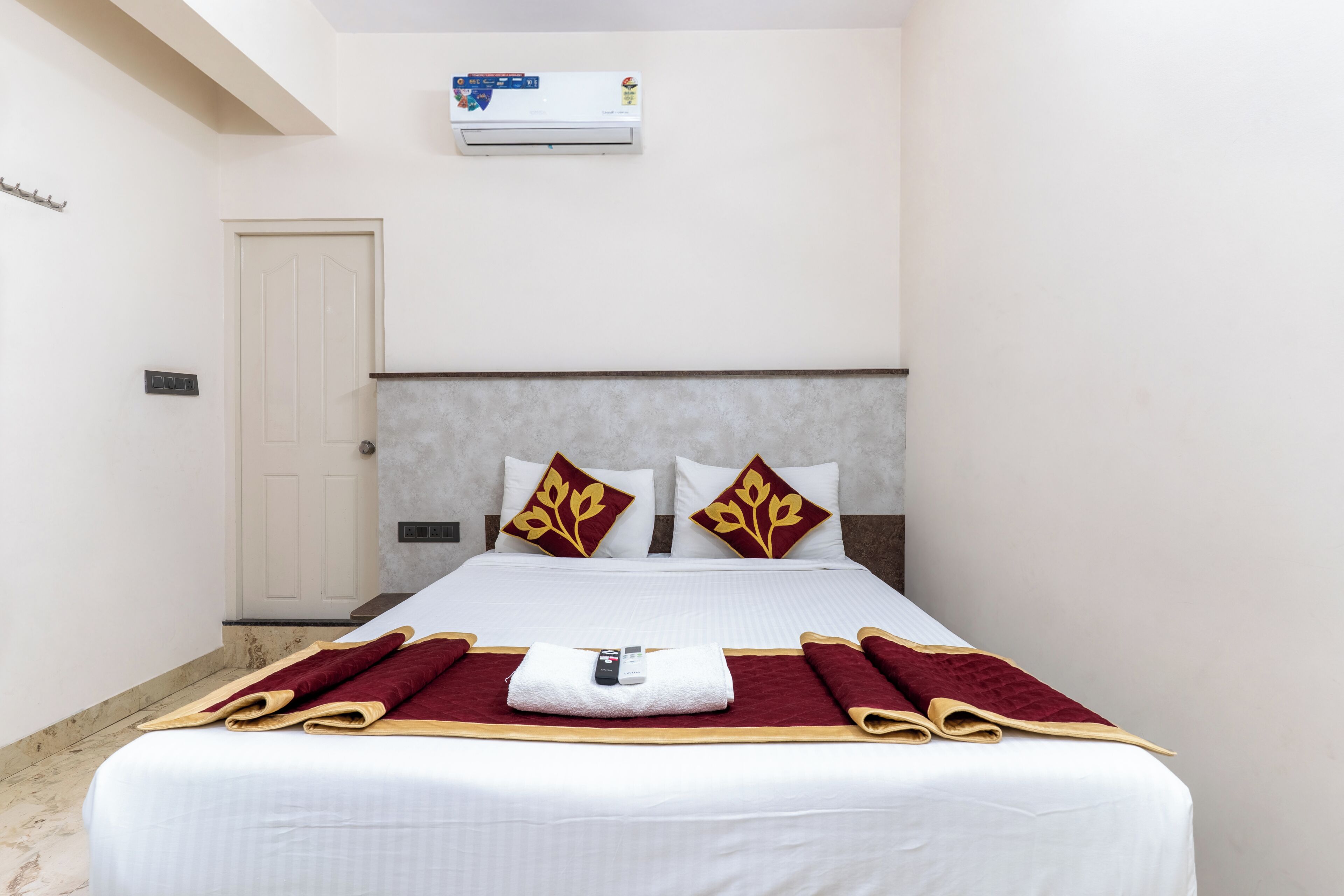 Ein Hotelzimmer mit einem Bett, einer Wandklimaanlage, einer Tür und einem Lichtschalter.