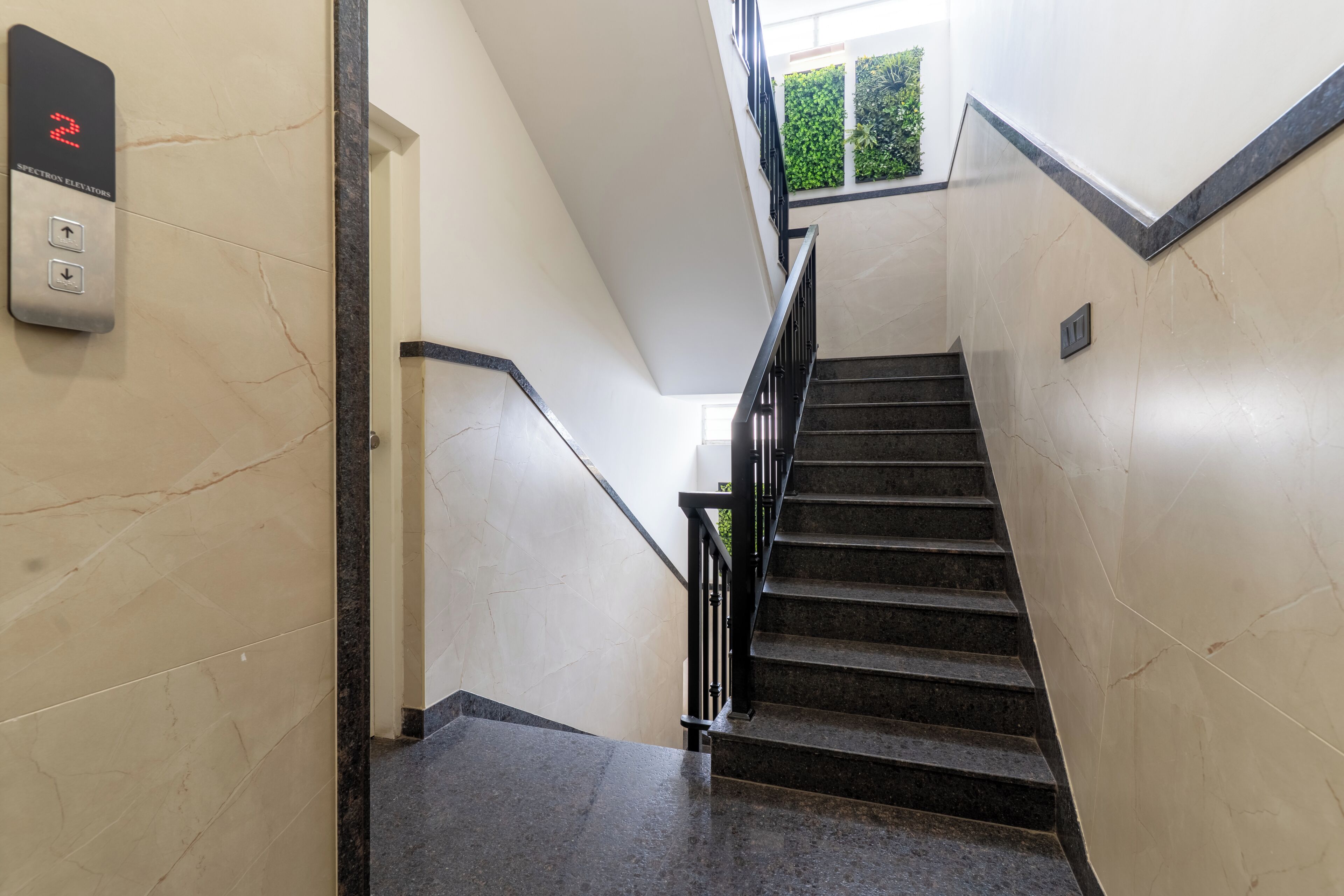 Un escalier avec une rampe, un panneau de commande d’ascenseur fixé au mur et une fenêtre en haut de l’escalier.