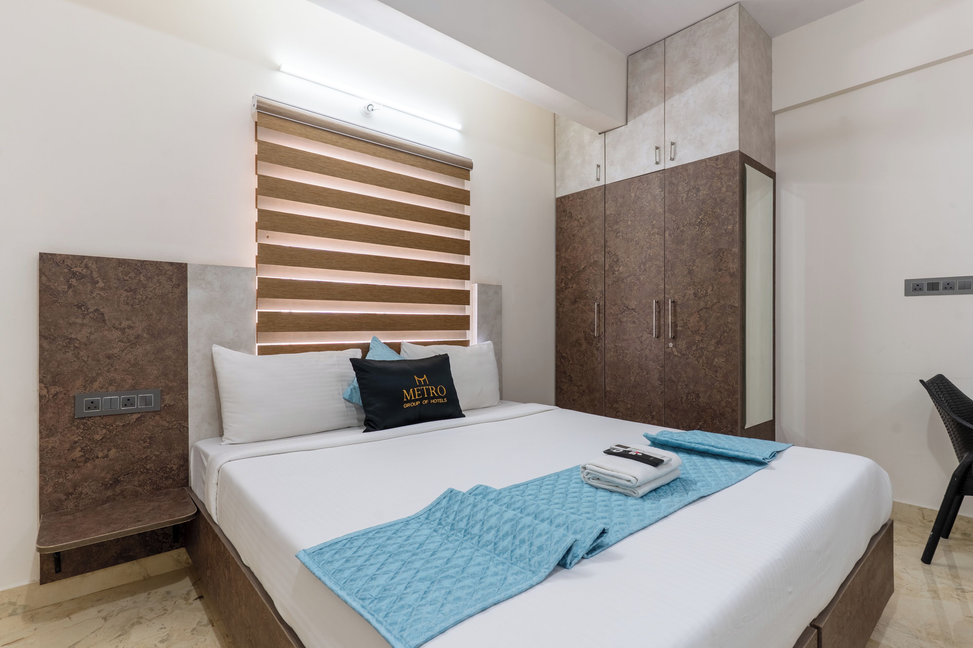 Habitació d'hotel amb llit, armari, escriptori i finestra amb persianes.