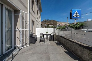 A balcony with outdoor furniture, a pedestrian crossing sign, and a view of buildings in the background. - KeyRoom • Patio & Parking near Lake Como (Como)