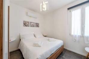 Ein Schlafzimmer mit einem Bett, weißen Vorhängen, einer Wandklimaanlage und Kunstwerken.