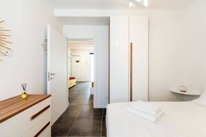 A modern bedroom with a wooden bedside table, a neatly made bed, and a white wardrobe. - KeyRoom • Patio & Parking near Lake Como (Como)