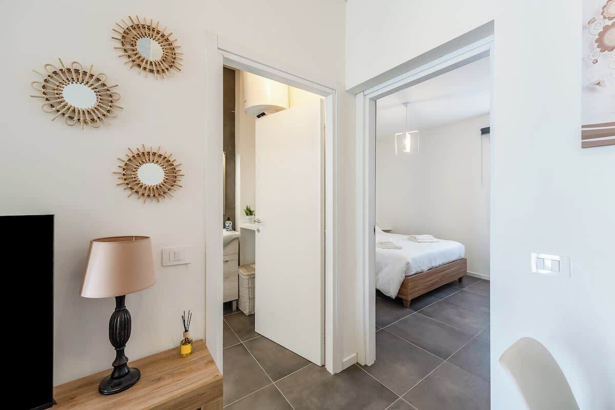A modern hotel room with a bed, a bedside table with a lamp, and a wall with decorative mirrors.