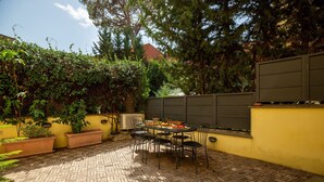 An outdoor patio with a table and chairs, surrounded by a yellow wall and greenery. - Garden & Private Entrance – Ponte Milvio Loft (Rome)