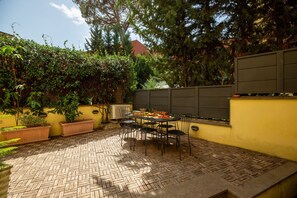 Eine Terrasse im Freien mit Tisch und Stühlen, umgeben von einer gelben Wand und Pflanzen.