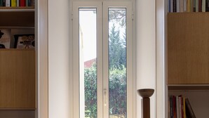 A room with a built-in bench, a window with a view of greenery, and bookshelves with books. - Garden & Private Entrance – Ponte Milvio Loft (Rome)