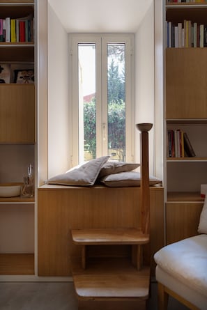 Ein Zimmer mit eingebauter Sitzbank, einem Fenster mit Blick ins Grüne und Bücherregalen voller Bücher.