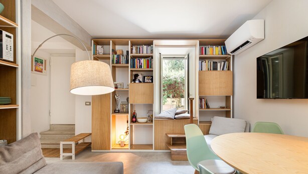 A modern living space with a dining area, bookshelves, and a view to the outdoors. - Garden & Private Entrance – Ponte Milvio Loft (Rome)