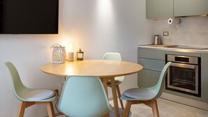 A modern kitchen with a round dining table, four chairs, a built-in oven, and a flat-screen TV mounted on the wall. - Garden & Private Entrance – Ponte Milvio Loft (Rome)
