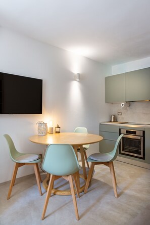 Eine moderne Küche mit einem runden Esstisch, vier Stühlen, einem Einbauofen und einem an der Wand befestigten Flachbildfernseher.