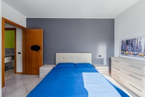 Ein Schlafzimmer mit einem Bett, einer Kommode, einer Tür und einer Wand mit Stadtbild-Gemälde.