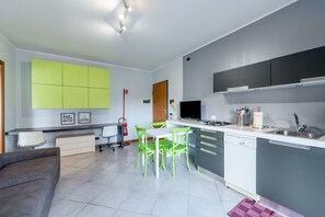 Eine moderne Küche mit Essbereich, mit einem weißen Tisch, grünen Stühlen und grauen Schränken.