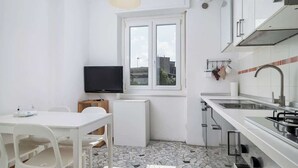A compact kitchen with white cabinetry, a tiled backsplash, a small window, and a television. - Porta Venezia Apt: 30s to Metro, Easy Airport (Milan)