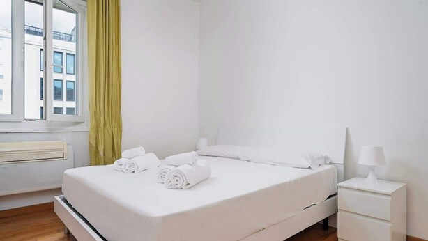A single-bed room with a window, a bedside table with a lamp, and neatly folded towels on the bed. - Porta Venezia Apt: 30s to Metro, Easy Airport (Milan)