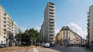 A multi-story building with balconies, a tram line, and parked cars on a city street. - Porta Venezia Apt: 30s to Metro, Easy Airport (Milan)