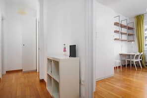 A modern interior with a wooden floor, white walls, a white cabinet with shelves, a small table with chairs, and a wall-mounted shelf unit. - Porta Venezia Apt: 30s to Metro, Easy Airport (Milan)