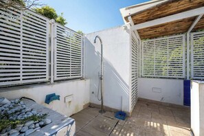 A small, enclosed outdoor area with a metal shower, a stone bench, and a white wall with a window. - Above the Ruins - a Dream of Baia (Bacoli)