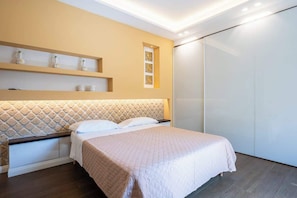 A modern bedroom with a bed, a headboard with a diamond pattern, a shelf with decorative items, and a sliding door closet. - Above the Ruins - a Dream of Baia (Bacoli)