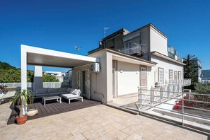 Een modern gebouw met een overdekt terras, een balkon en uitzicht op het omliggende landschap.