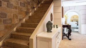 A staircase with stone walls, a white console table with a Buddha statue, and a view into a kitchen area. - Above the Ruins - a Dream of Baia (Bacoli)