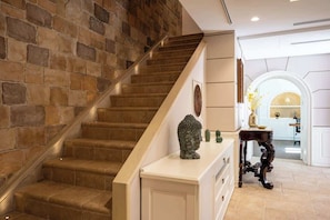 A staircase with stone walls, a white console table with a Buddha statue, and a view into a kitchen area. - Above the Ruins - a Dream of Baia (Bacoli)