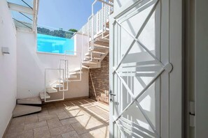 Un interior modern amb una escala que condueix a un balcó, una porta blanca i una vista del cel blau.