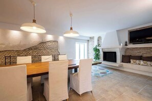 A dining area with a wooden table and chairs, a stone accent wall, and a fireplace with a TV above it. - Above the Ruins - a Dream of Baia (Bacoli)