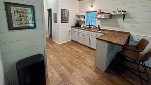 Une cuisine avec des meubles de rangement en bois, un plan de travail, un évier et une fenêtre avec des stores.