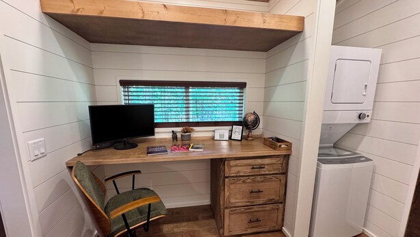 Una habitación compacta con escritorio de madera, monitor de computadora, una silla, un globo terráqueo y lavadora integrada.