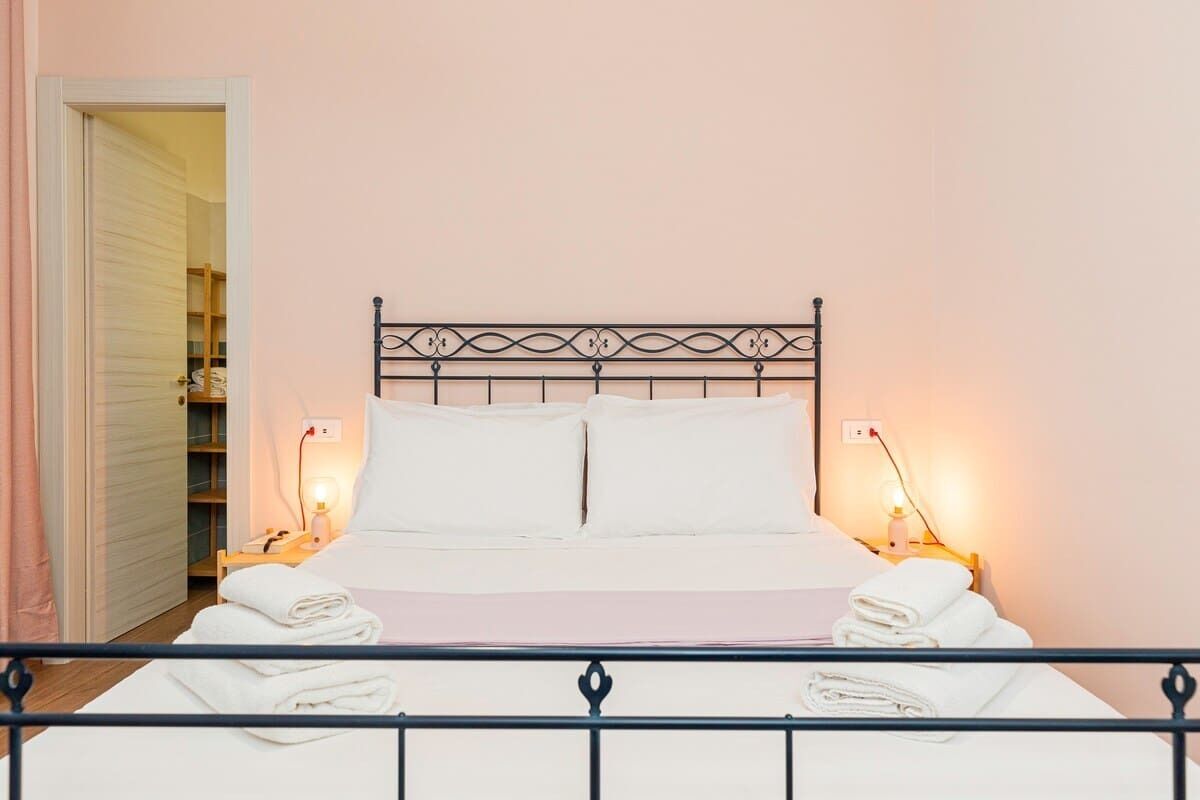 A neatly made bed with white linens, a metal headboard, and bedside lamps.