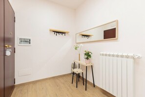 Ein Zimmer mit Holzboden, Heizkörper, Schreibtisch mit Stuhl, Spiegel und einer Topfpflanze.