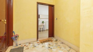 A hallway with a yellow wall, a wooden door, and a tiled floor. - Comfy&Stylish Apt in Rome (Rome)