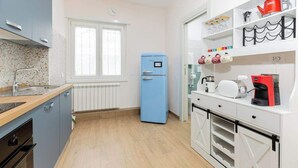 A modern kitchen with a blue refrigerator, white cabinets, and a countertop with a coffee machine. - Comfy&Stylish Apt in Rome (Rome)