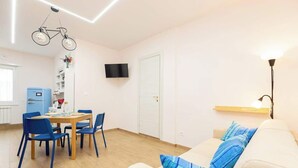 A room with a dining table, chairs, a sofa, a television, and a wall-mounted light fixture. - Comfy&Stylish Apt in Rome (Rome)