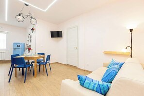 A room with a dining table, chairs, a sofa, a television, and a wall-mounted light fixture. - Comfy&Stylish Apt in Rome (Rome)