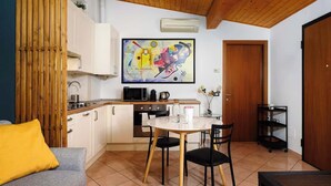 A compact kitchen with white cabinets, a dining table with chairs, a sofa with a yellow pillow, and a wooden ceiling. - Modern Apartment Near Centrale Station (Milan)
