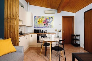 A compact kitchen with white cabinets, a dining table with chairs, a sofa with a yellow pillow, and a wooden ceiling. - Modern Apartment Near Centrale Station (Milan)