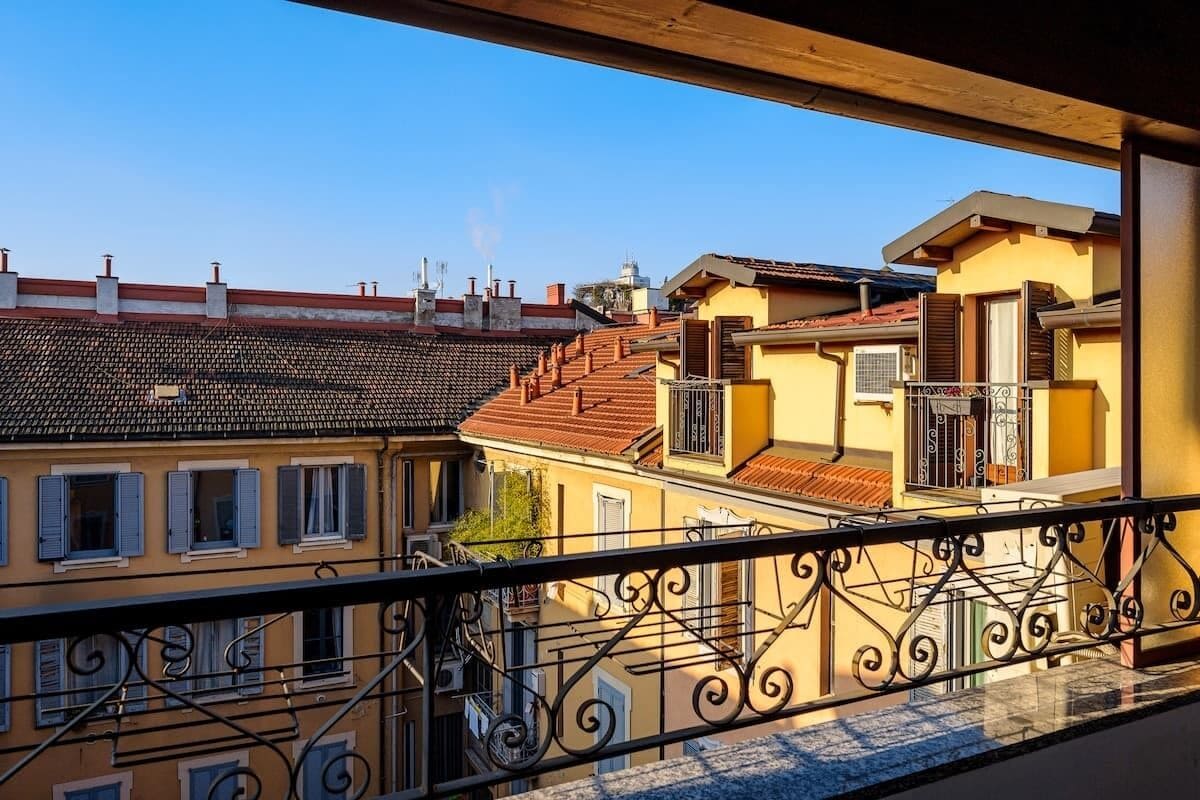 A balcony with wrought iron railings overlooking a row of terracotta-roofed buildings with balconies.