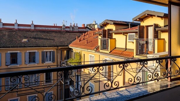 A balcony with wrought iron railings overlooking a row of terracotta-roofed buildings with balconies. - Modern Apartment Near Centrale Station (Milan)