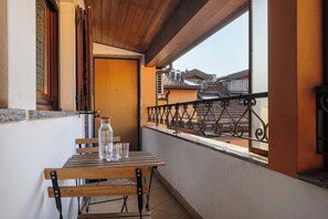 Een balkon met een houten tafel, stoelen, een fles en glazen.