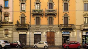A multi-story building with ornate balconies and a row of parked cars in front. - Modern Apartment Near Centrale Station (Milan)