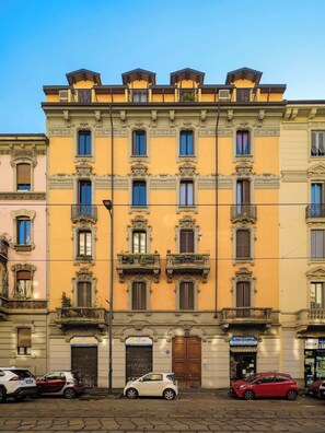 A multi-story building with ornate balconies and a row of parked cars in front. - Modern Apartment Near Centrale Station (Milan)