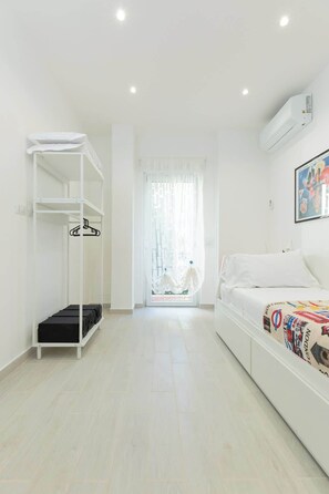 Ein schlicht eingerichtetes Hotelzimmer mit einem Bett, einem Schrank und einem durch eine Glastür einsehbaren Badezimmer.