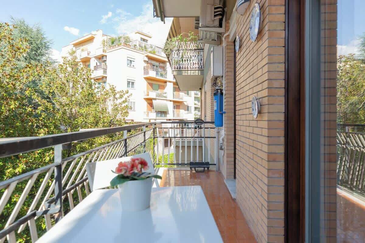 Un balcon avec une table, un pot de fleurs et une vue sur des immeubles à plusieurs étages.
