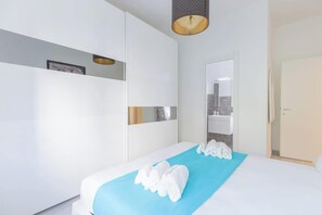 A hotel room with a bed, a blue towel on the bed, a white wall, and a door. - Holi Rome - Bright&Comfy apt inTrastevere (Rome)