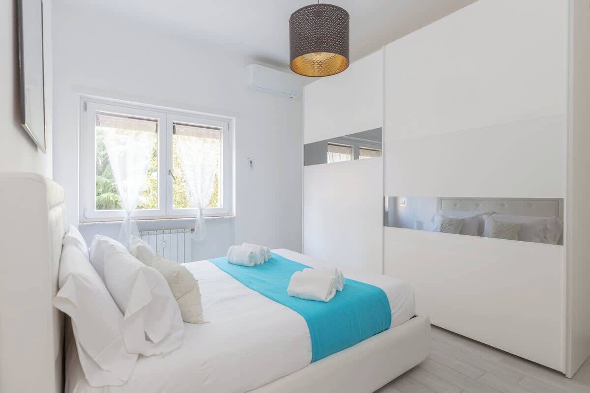 A bedroom with a bed, a window, a wardrobe, and a hanging light fixture.