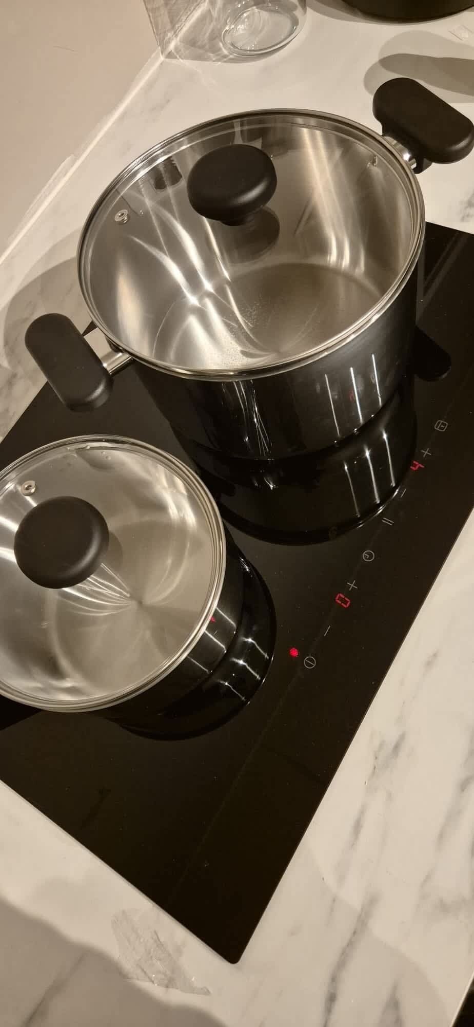 Zwei Edelstahl-Töpfe mit Deckeln auf einer schwarzen Induktionskochplatte.